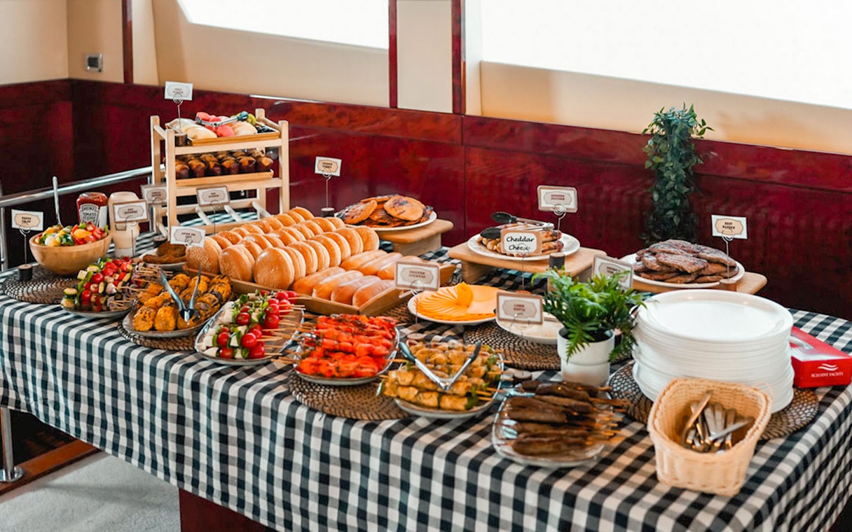 Breakfast buffet on a luxury yacht cruise with assorted pastries, fruits, and skewers.