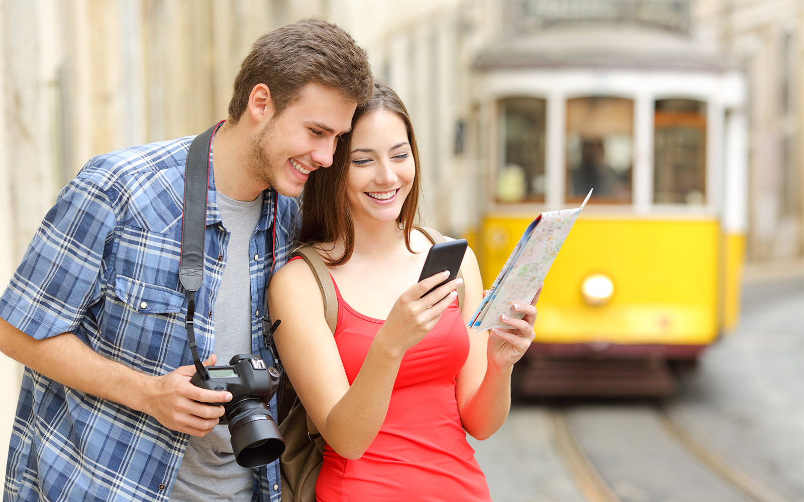 Tourists exploring Lisbon with a map and camera near a yellow tram.
