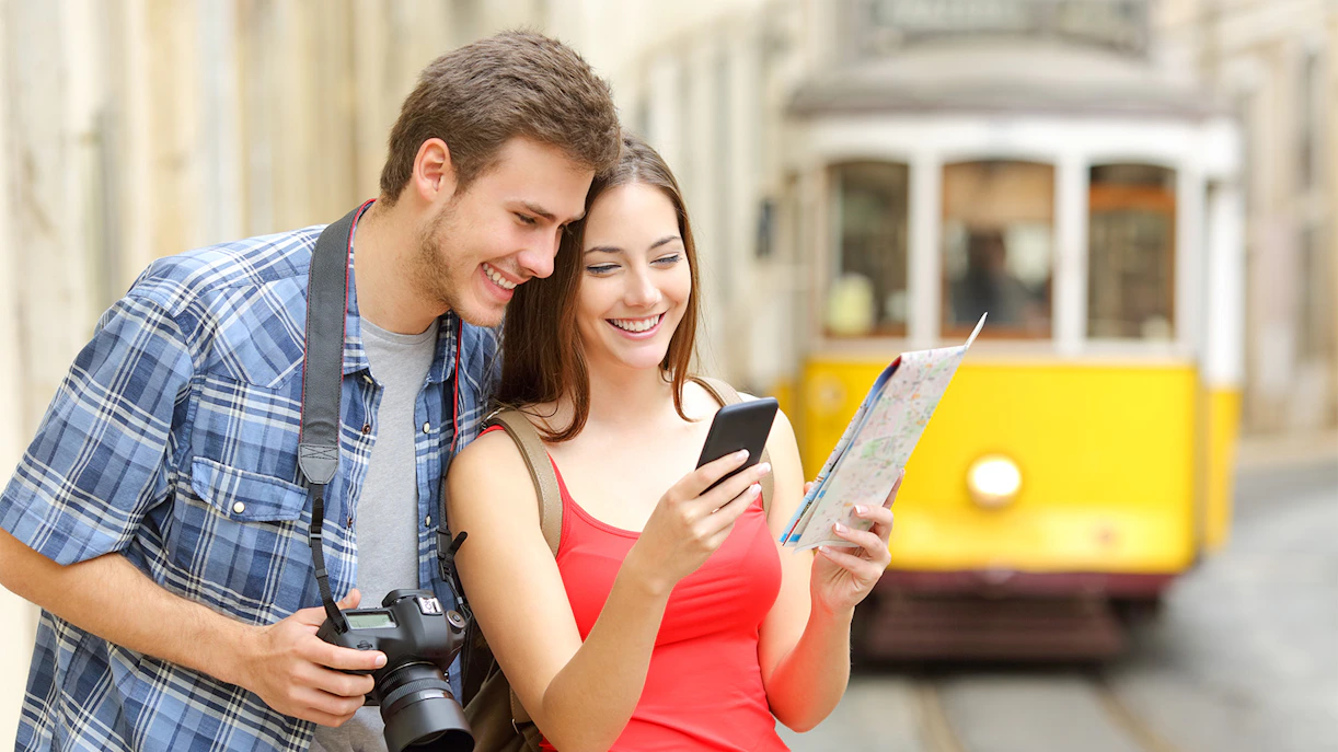 Tourists exploring Lisbon with a map and camera near a yellow tram.