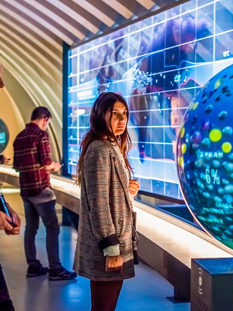 Tourists at Cité du Vin museum in Bordeaux using audio guides near interactive wine exhibit.