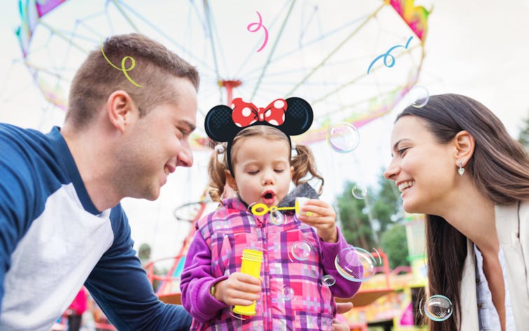 Family enjoying bubble play at an amusement park with a Ferris wheel in the background.