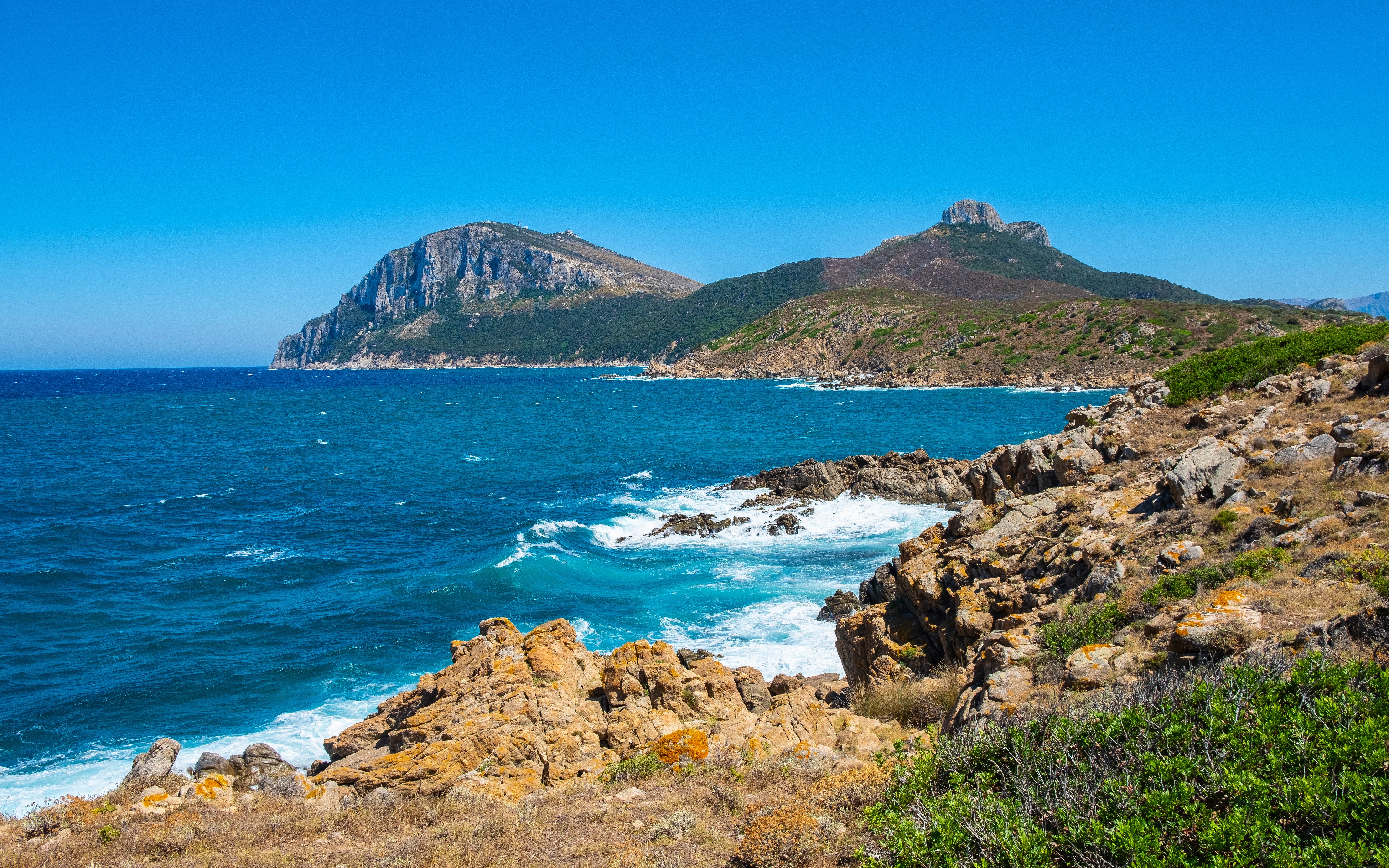 Capo Figari cape cliffs with rocky shoreline and blue sea in Sardinia, Italy.