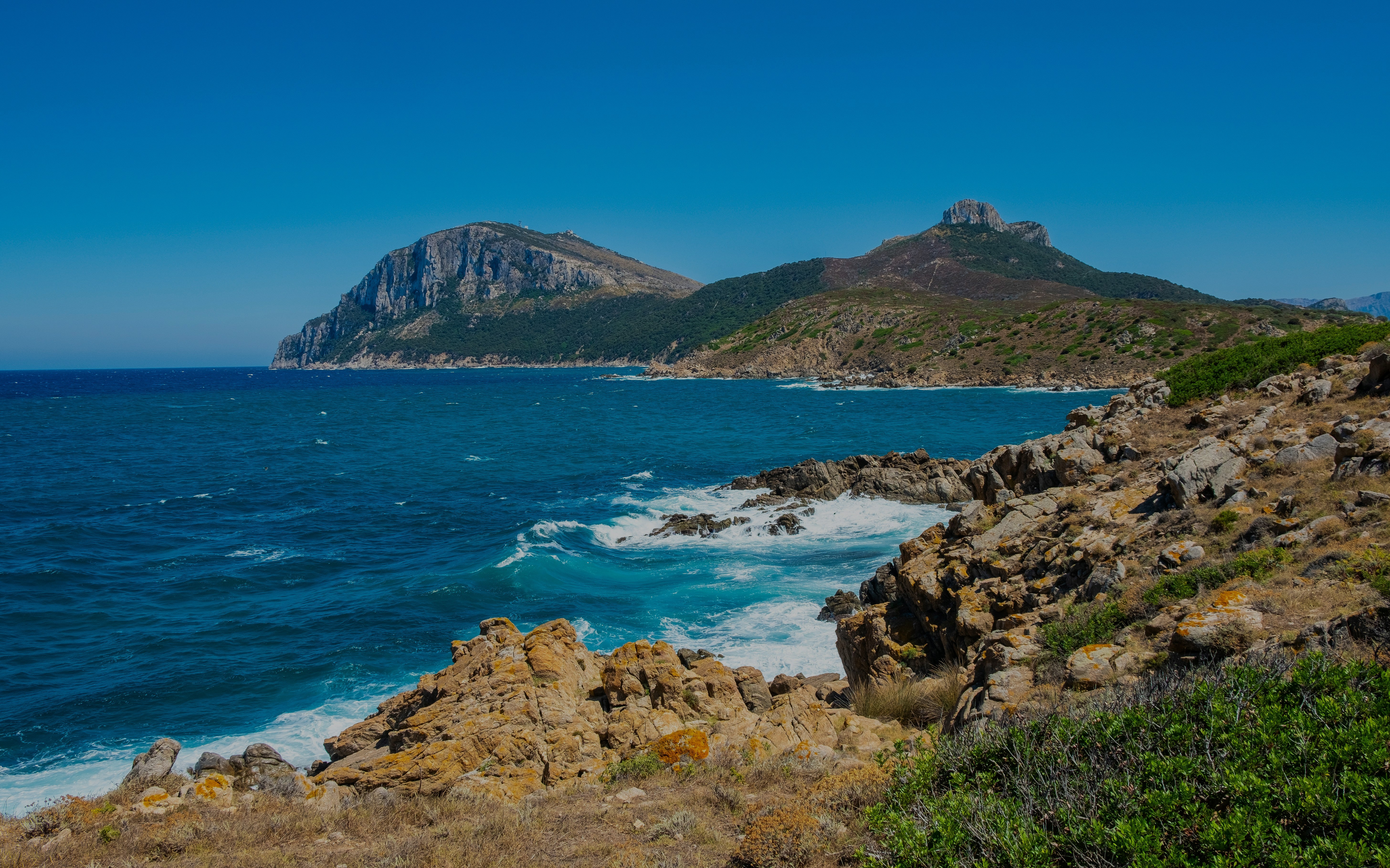 Capo Figari cape cliffs with rocky shoreline and blue sea in Sardinia, Italy.