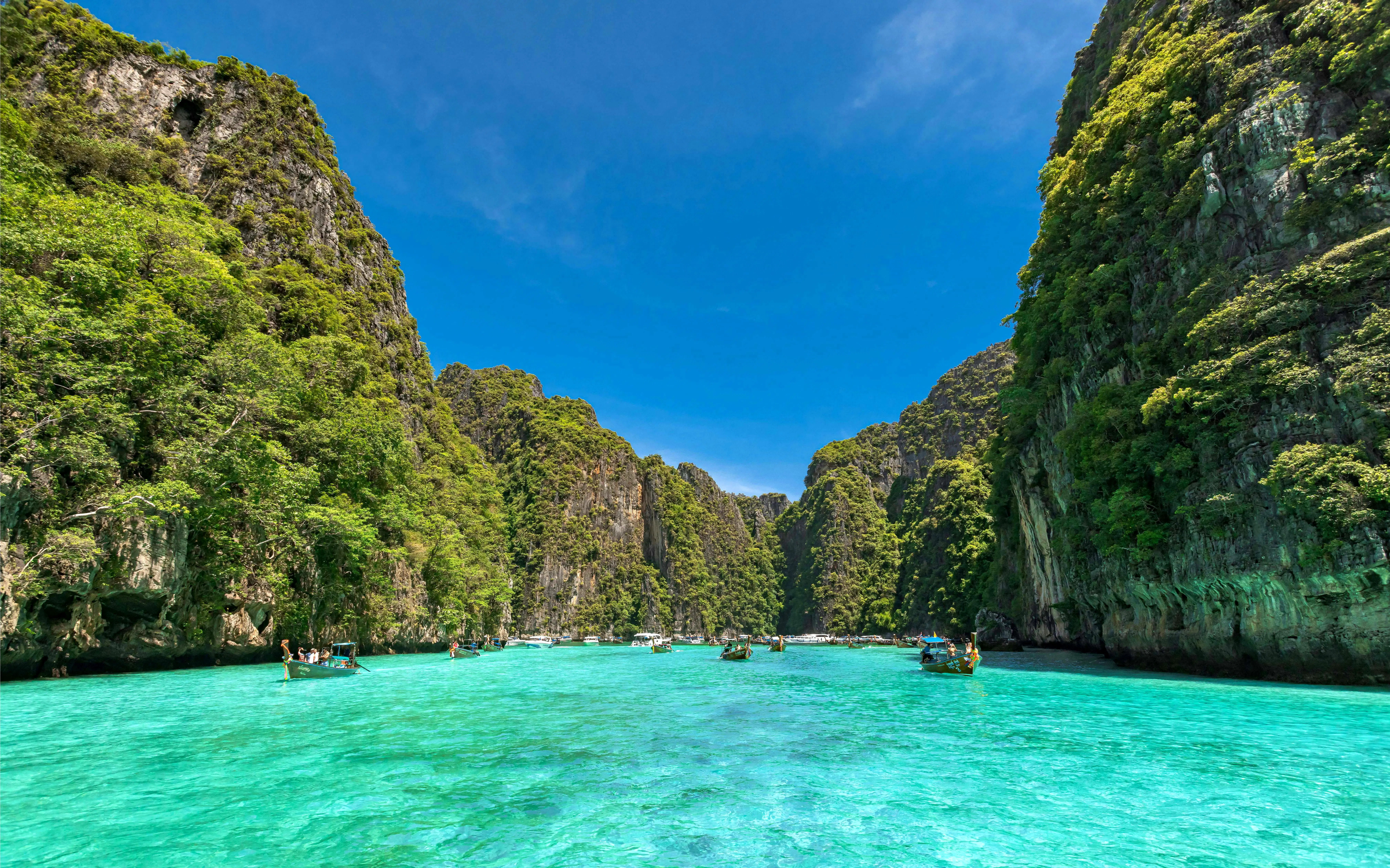 Speedboats on turquoise waters between lush cliffs, Phi Phi Islands, Phuket tour.