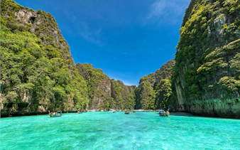 Speedboats on turquoise waters between lush cliffs, Phi Phi Islands, Phuket tour.