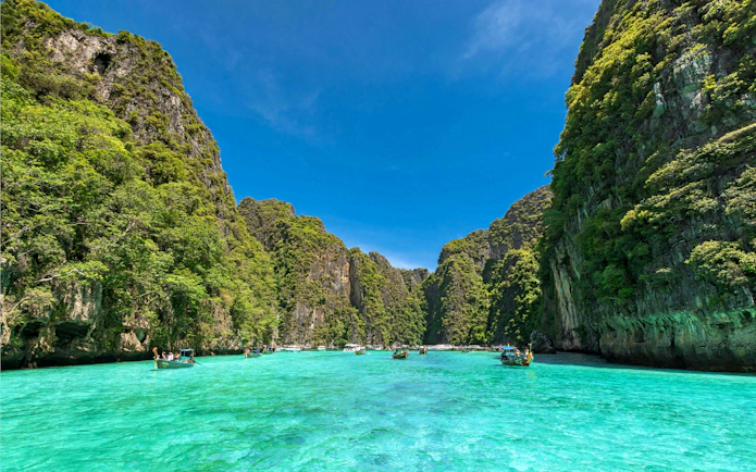 Speedboats on turquoise waters between lush cliffs, Phi Phi Islands, Phuket tour.
