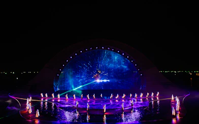 Performers in illuminated costumes at the Kiss of the Sea Show with vibrant water and light display.
