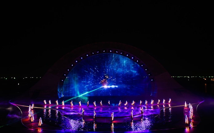 Performers in illuminated costumes at the Kiss of the Sea Show with vibrant water and light display.