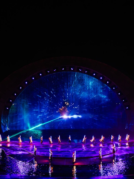 Performers in illuminated costumes at the Kiss of the Sea Show with vibrant water and light display.