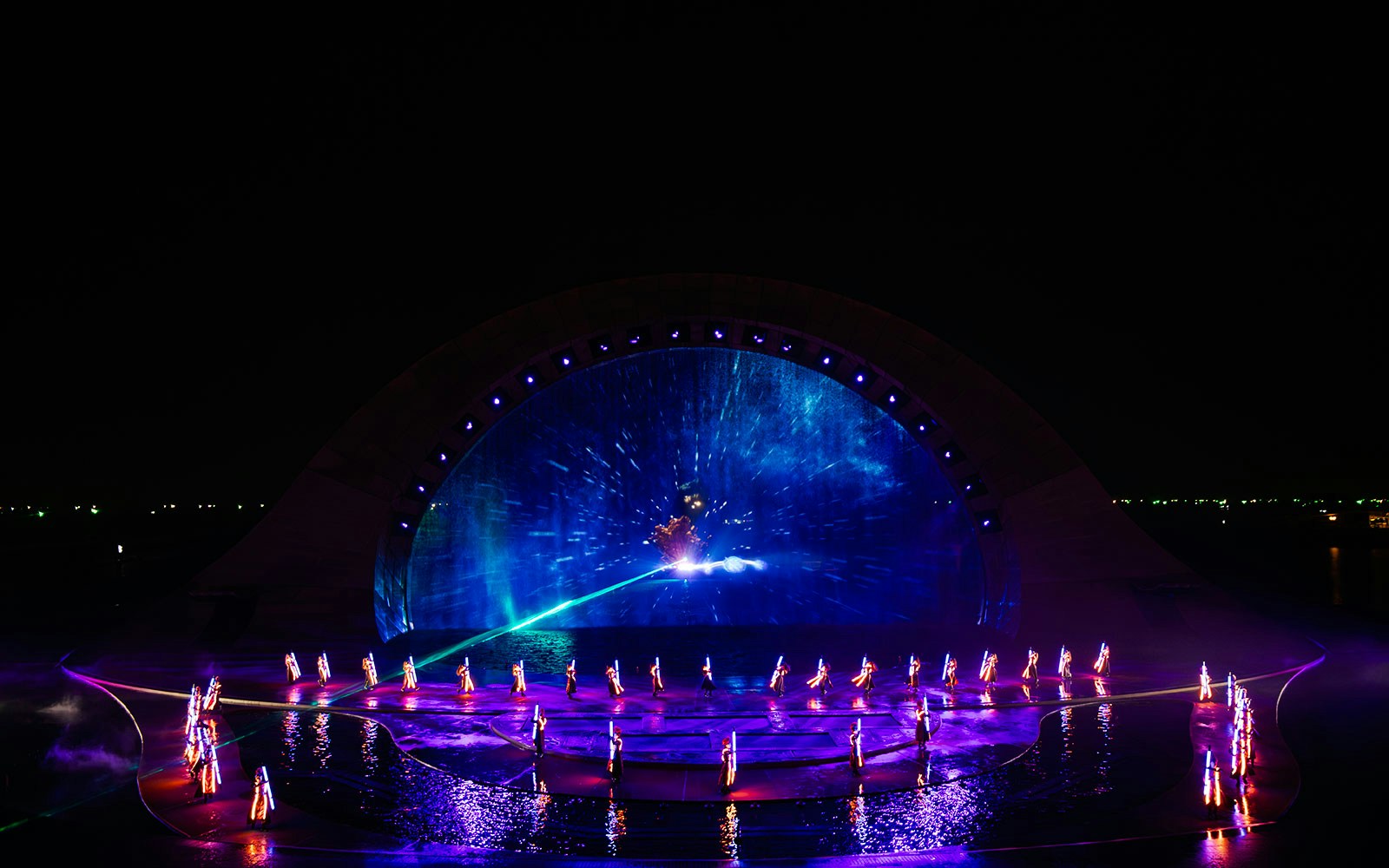 Performers in illuminated costumes at the Kiss of the Sea Show with vibrant water and light display.