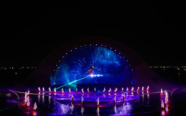 Performers in illuminated costumes at the Kiss of the Sea Show with vibrant water and light display.
