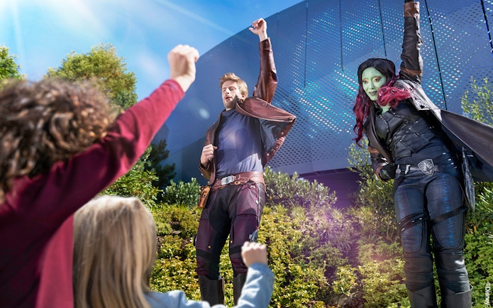 Characters in costume interacting with children at a theme park attraction.