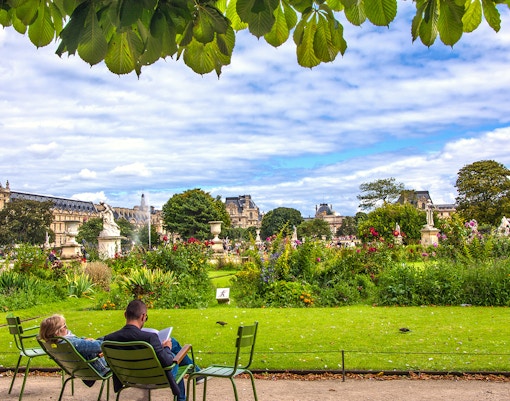 Visitors relaxing in Tuileries Garden, Paris, with historic buildings and statues in the background.