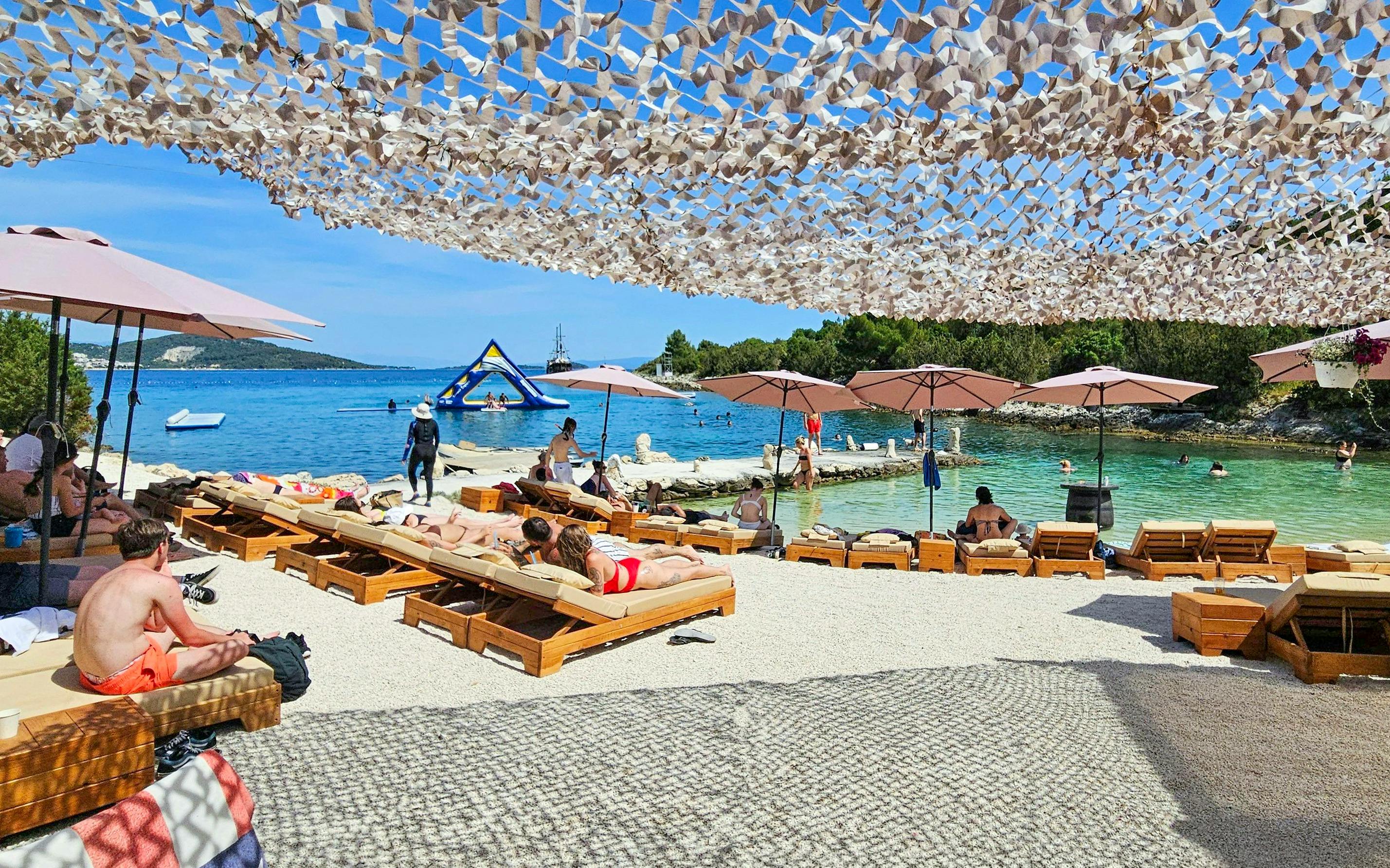 Sunbathers at a beach resort with umbrellas and a view of the sea and inflatable water park.