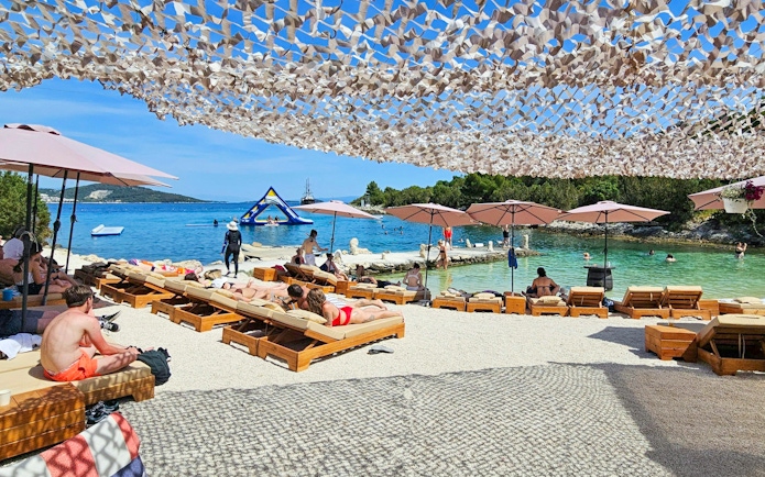 Sunbathers at a beach resort with umbrellas and a view of the sea and inflatable water park.