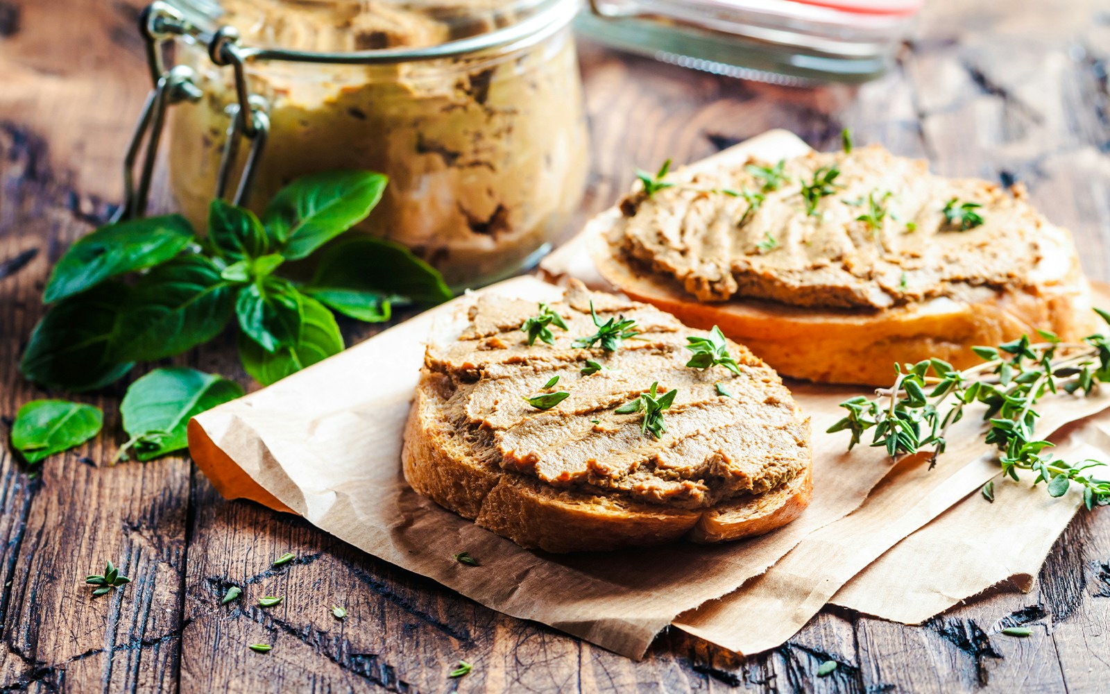Fresh chicken liver pate served on a wooden board with bread slices and herbs.