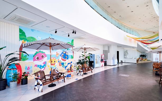 Indoor seating area with colorful mural at Busan X The SKY, featuring beach-themed cartoon characters.