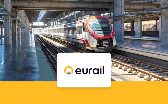 Eurail train crossing scenic European countryside with mountains and fields in view.