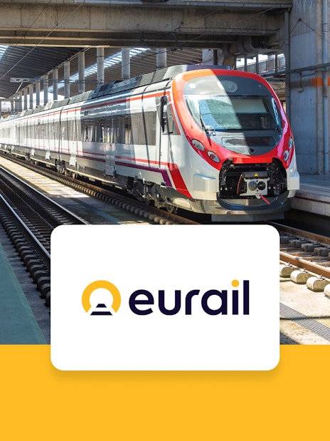 Eurail train crossing scenic European countryside with mountains and fields in view.