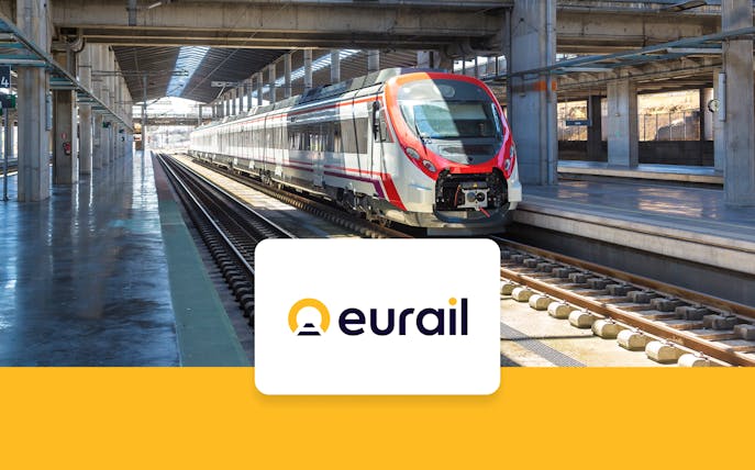 Eurail train crossing scenic European countryside with mountains and fields in view.