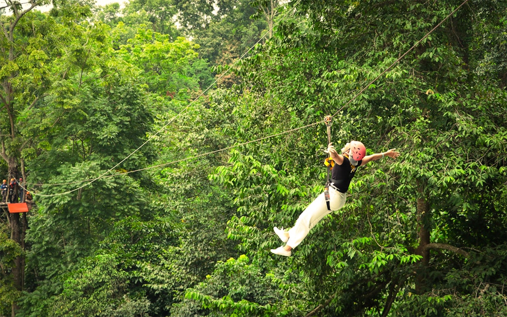 Woman ziplining with arms outstretched over jungle canopy in Pongyang, Chiang Mai.
