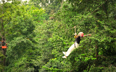 Woman ziplining with arms outstretched over jungle canopy in Pongyang, Chiang Mai.