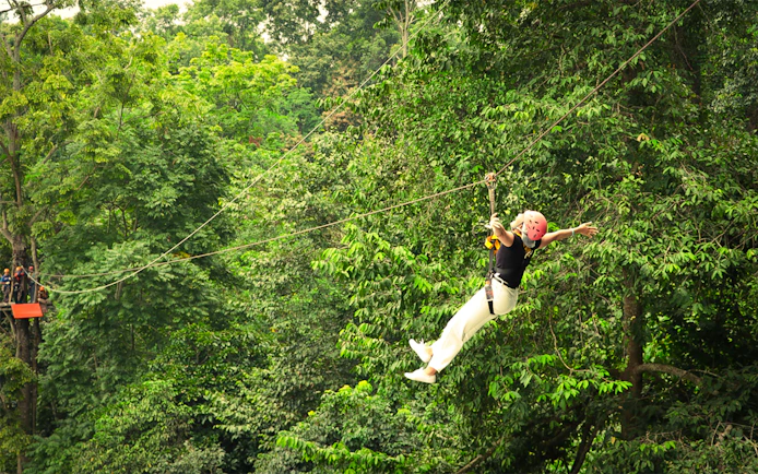 Woman ziplining with arms outstretched over jungle canopy in Pongyang, Chiang Mai.