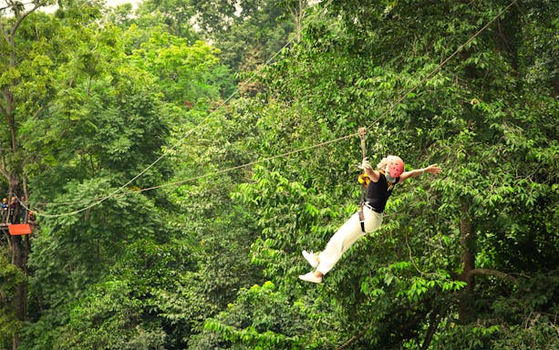 Woman ziplining with arms outstretched over jungle canopy in Pongyang, Chiang Mai.