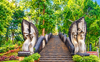 Stone staircase with ornate Naga sculptures in lush greenery, Chiang Rai, Thailand.