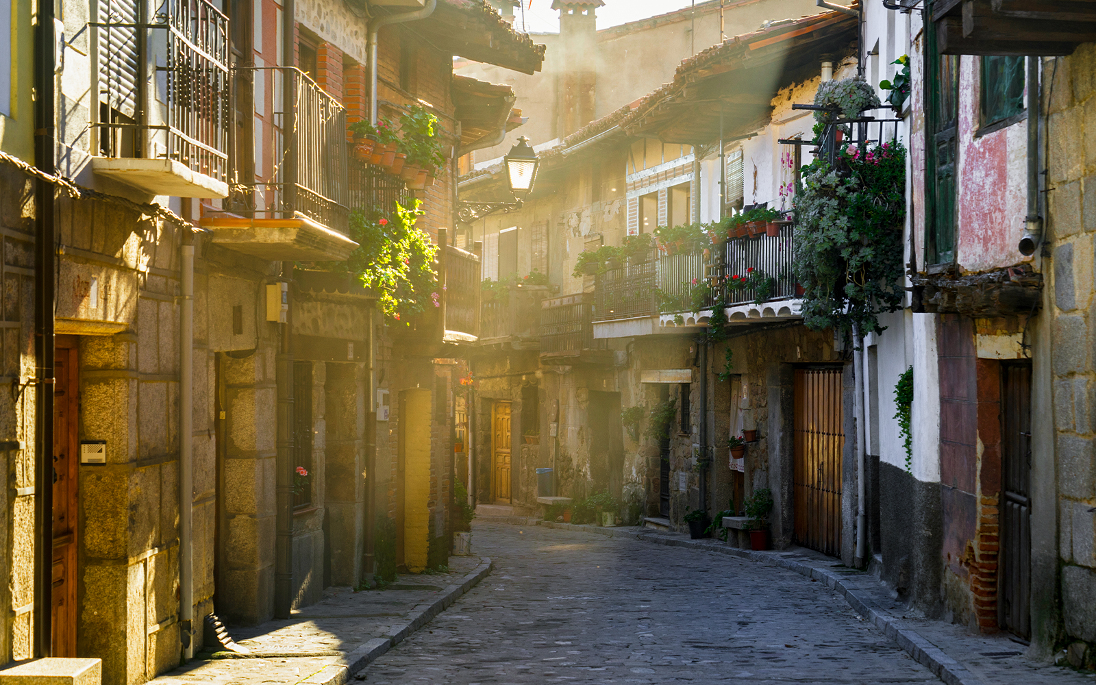 Narrow cobblestone street in Cuevas del Valle, Avila, with rustic buildings at sunset.