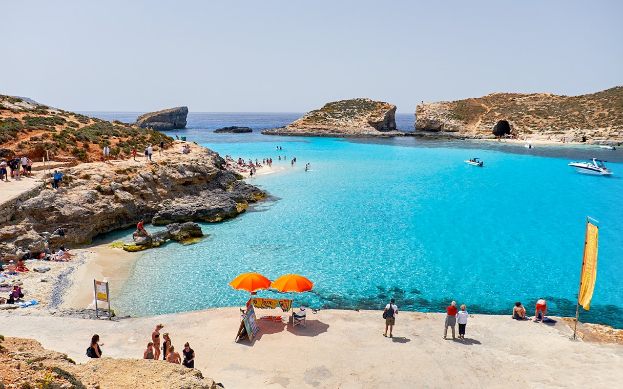 Visitors enjoying the clear waters of Blue Lagoon, Malta with boats and rocky cliffs in the background.
