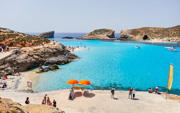 Visitors enjoying the clear waters of Blue Lagoon, Malta with boats and rocky cliffs in the background.