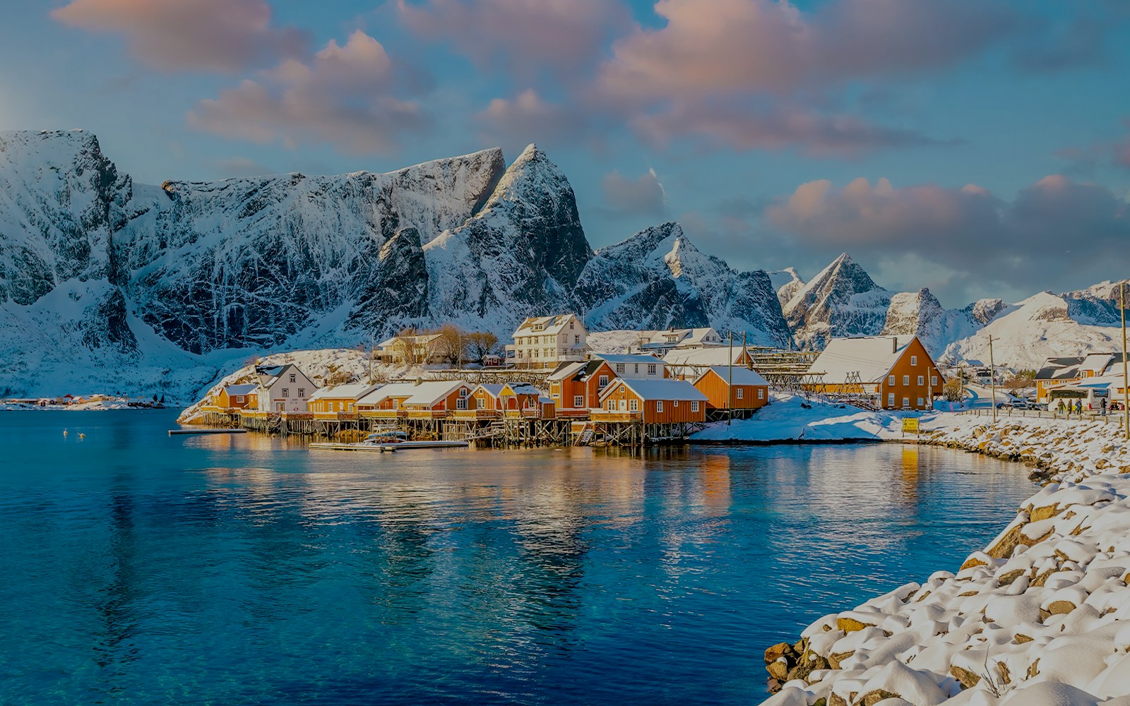Lofoten Norway winter landscape with snow-covered mountains and orange coastal houses.