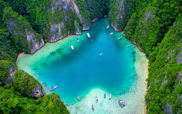 Aerial view of boats in turquoise waters surrounded by lush cliffs at Phi Phi Islands, Thailand.