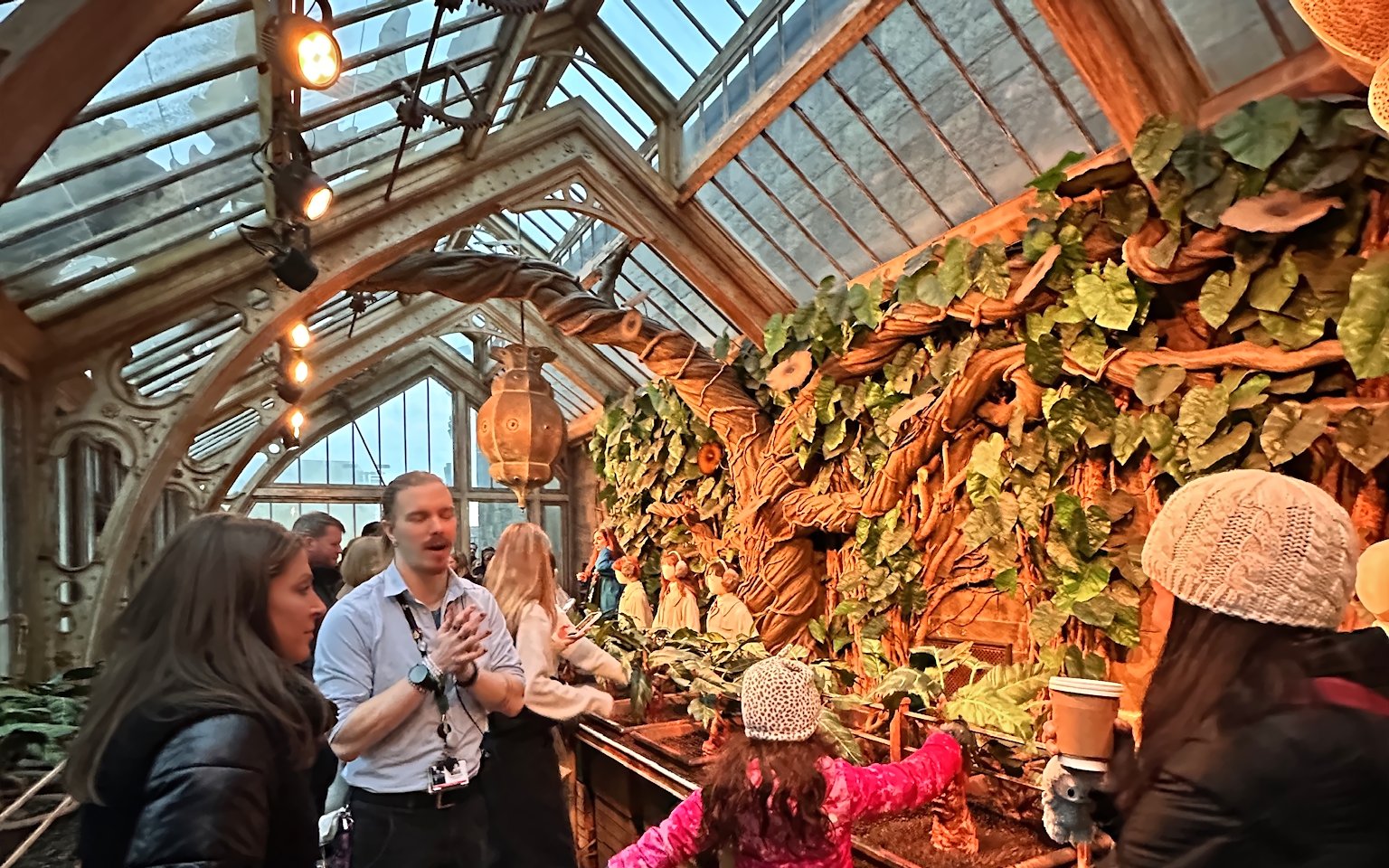 Visitors exploring Professor Sprout's greenhouse with large plants and intricate architecture.