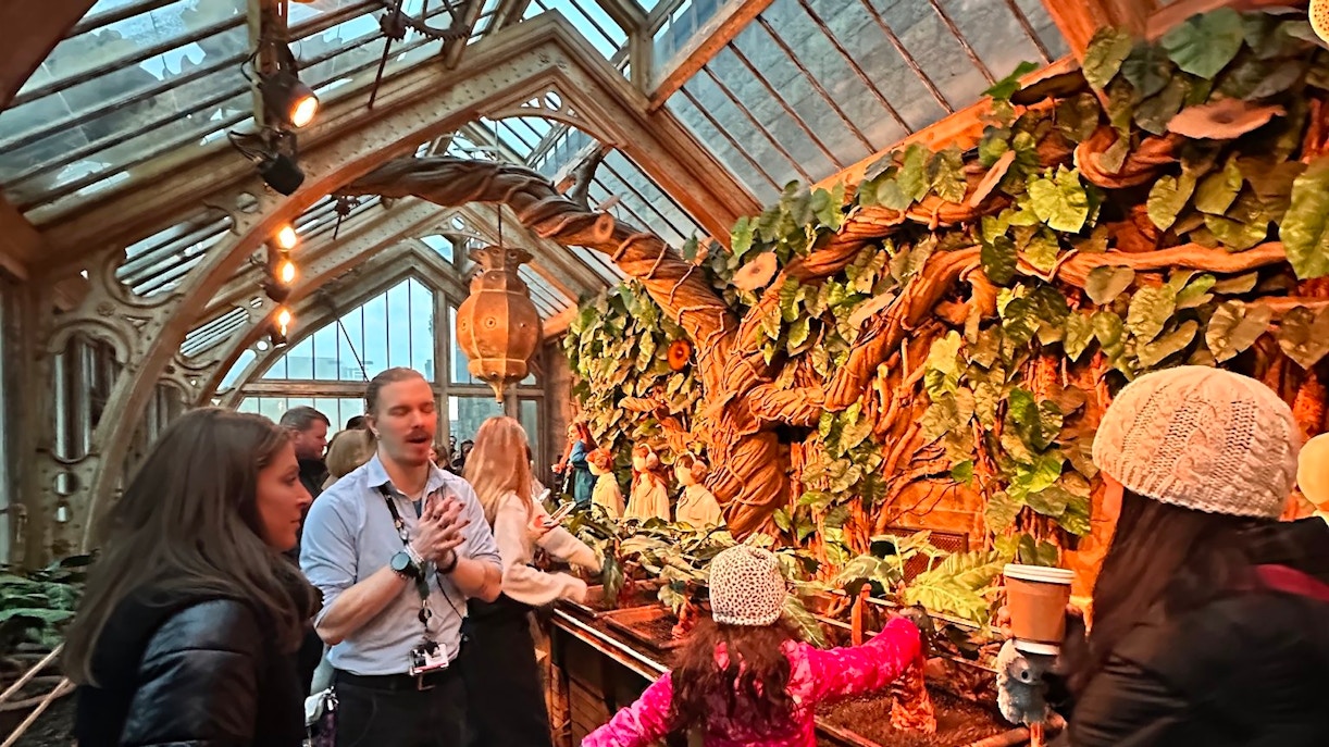 Visitors exploring Professor Sprout's greenhouse with large plants and intricate architecture.