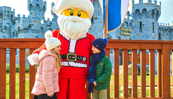 Children meeting Lego Santa at Legoland Christmas, London with castle backdrop.