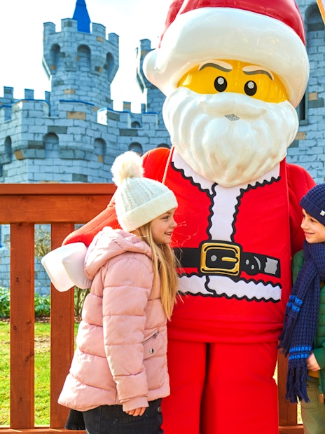 Children meeting Lego Santa at Legoland Christmas, London with castle backdrop.