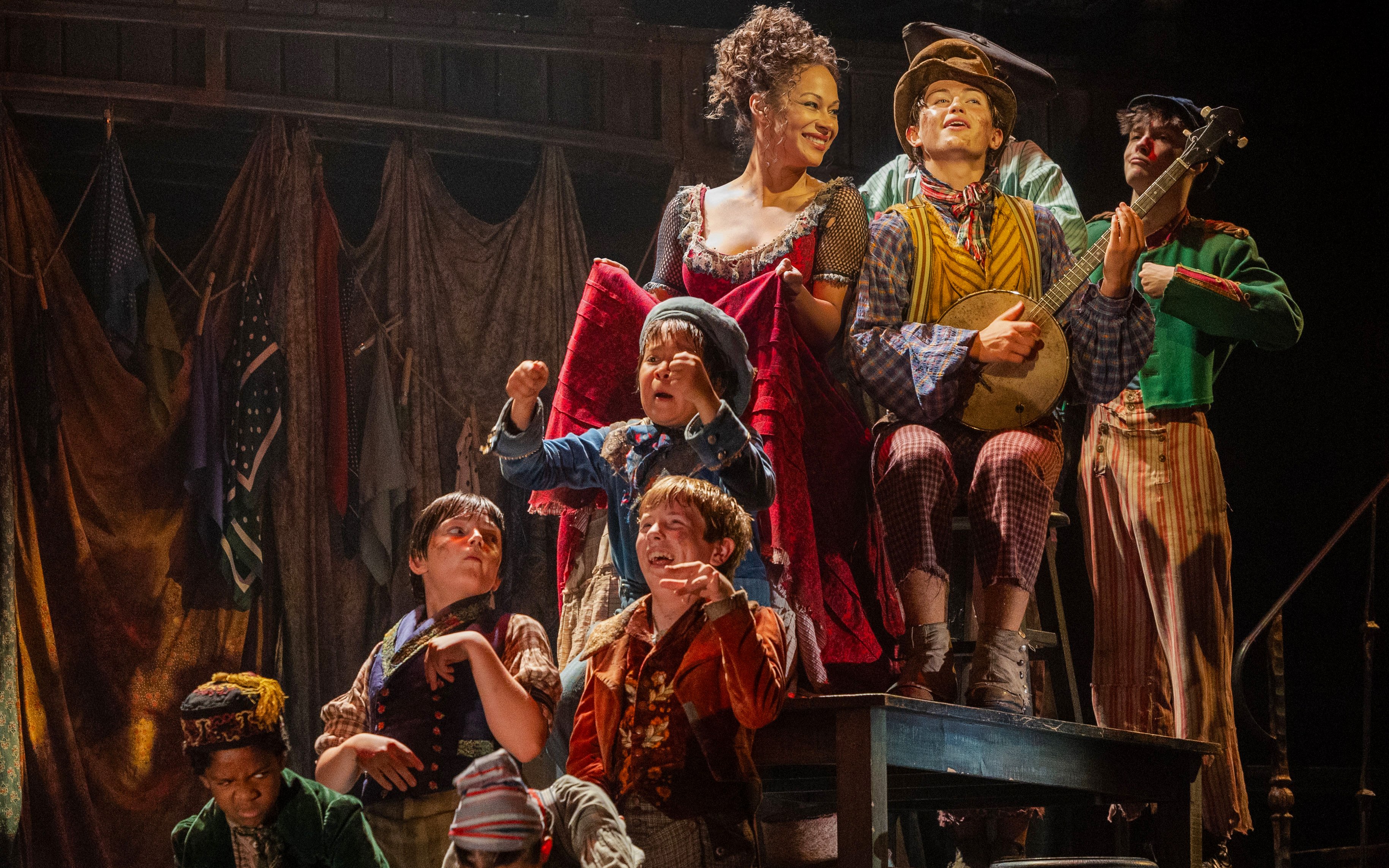 Cast performing a lively scene from the musical "Oliver" with period costumes and props.