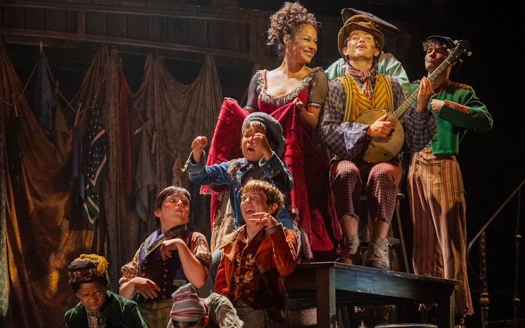 Cast performing a lively scene from the musical "Oliver" with period costumes and props.