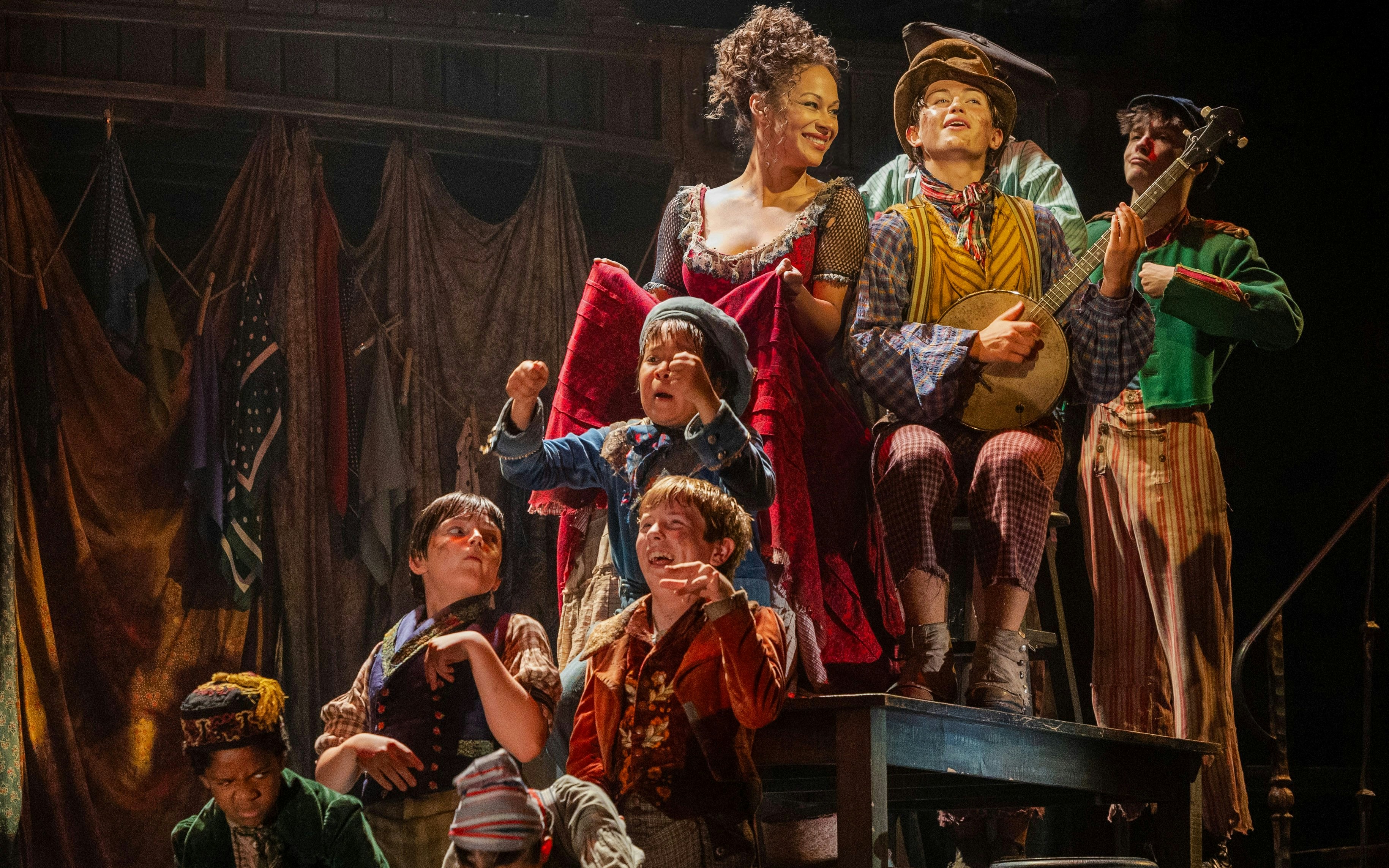 Cast performing a lively scene from the musical "Oliver" with period costumes and props.