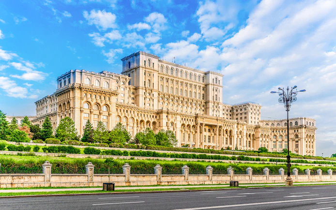 Romanian Parliament building in Bucharest with gardens and clear sky.