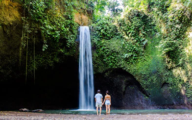 Visitors standing in front of Tibumana Waterfall surrounded by lush greenery in Bali, Indonesia.