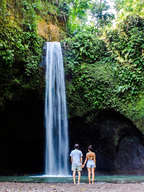 Visitors standing in front of Tibumana Waterfall surrounded by lush greenery in Bali, Indonesia.