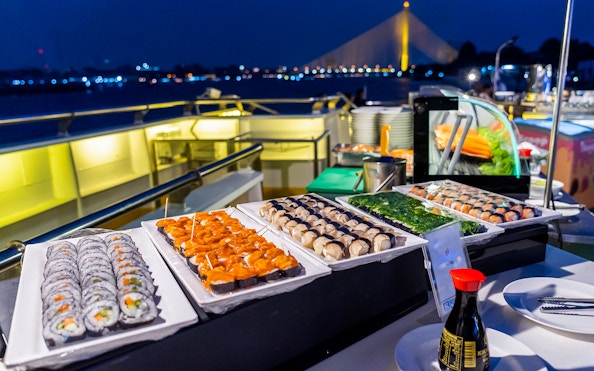 Sushi buffet on a cruise ship with a view of a lit-up bridge at night.