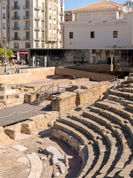 Roman Theater ruins in Málaga with nearby modern buildings and tourists exploring.