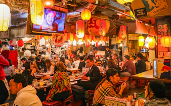 Patrons enjoying food and drinks at a bustling local izakaya bar in Japan.