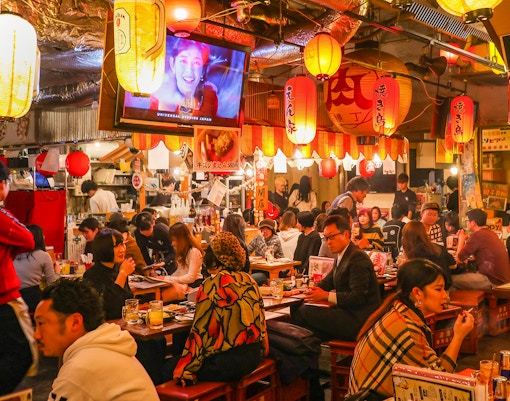 Patrons enjoying food and drinks at a bustling local izakaya bar in Japan.