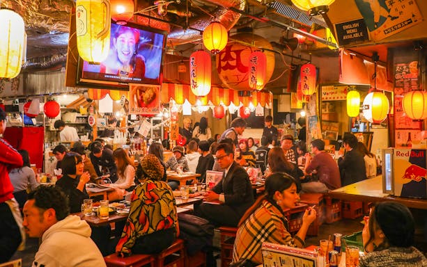 Patrons enjoying food and drinks at a bustling local izakaya bar in Japan.