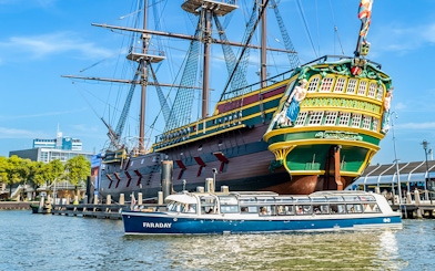 Canal cruise boat passing a historic ship in Amsterdam harbor.